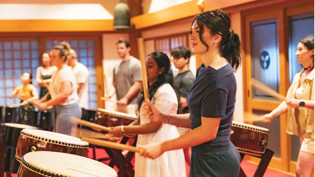 Foreign visitors in Japan enjoying a hands-on taiko drum workshop, hitting Japanese drums and experiencing traditional taiko performance as a cultural activity.